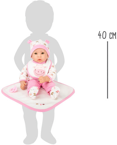 Die 40 cm große Puppe „Hanna“, in Rosa und Weiß gekleidet, sitzt auf einer Matte, neben ihr steht zum Größenvergleich eine Kindersilhouette.
