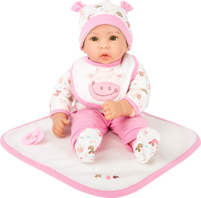 Puppe „Hanna“, Babypuppe in einem rosa-weißen Kuh-Outfit mit passender Mütze, sitzt auf einer rosa eingefassten Decke und hält einen Schnuller.