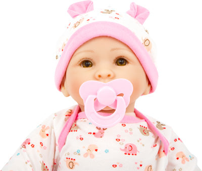 Puppe „Hanna“ ist eine Babypuppe, die eine rosa-weiße Mütze und einen bedruckten Pyjama trägt und einen rosa Schnuller im Mund hält.