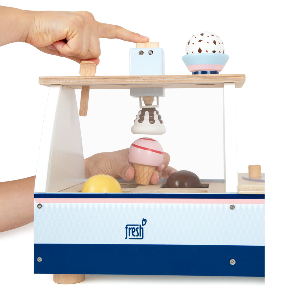 Eine Hand drückt einen Holzhebel an der Eistheke „fresh“, einer Spielzeug-Eismaschine mit Spielkugeln und Waffel.