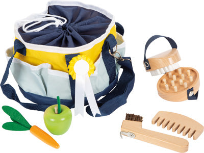Die Pferdepflege-Tasche ist ein Spielzeug-Pflegeset, das eine Tasche, eine Holzbürste, einen Kamm, einen Striegel, einen grünen Apfel und eine Filzkarotte enthält.