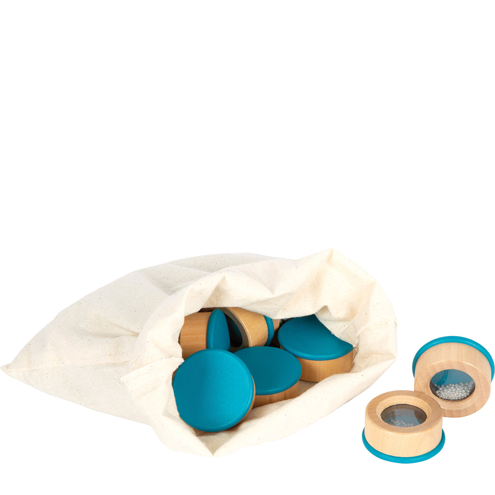 Das Hörmemo „Sensory“ besteht aus einem Stoffbeutel, gefüllt mit Holzscheiben – teilweise mit blauem Deckel – und zwei geöffneten Scheiben, hinter denen sich kleine Gegenstände befinden.