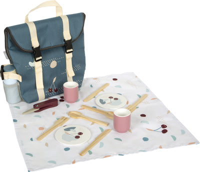 Der Picknickrucksack „Tasty“ umfasst Teller, Tassen, Besteck und Serviette in einem blauen Rucksack, alles angeordnet auf einem gemusterten Tuch.