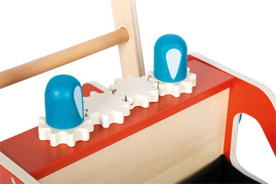 Nahaufnahme von zwei blauen Holzknöpfen auf weißen Zahnrädern auf dem roten und hölzernen Lauflernwagen der Feuerwehr, mit einem Holzgriff dahinter.
