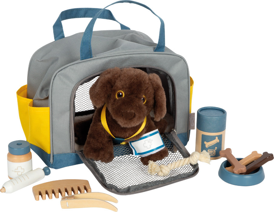 Das „Hund mit Tasche und Pflege“-Set besteht aus einem braunen Plüschhund in einer grauen Tragetasche, umgeben von Spielzeug-Pflegewerkzeugen, Knochen und Tierpflegezubehör.