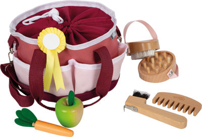 Ein Spielzeug-Pflegeset mit Tasche, Schleife, Bürste, Striegel, Holzkarotte, Apfel und Kamm.