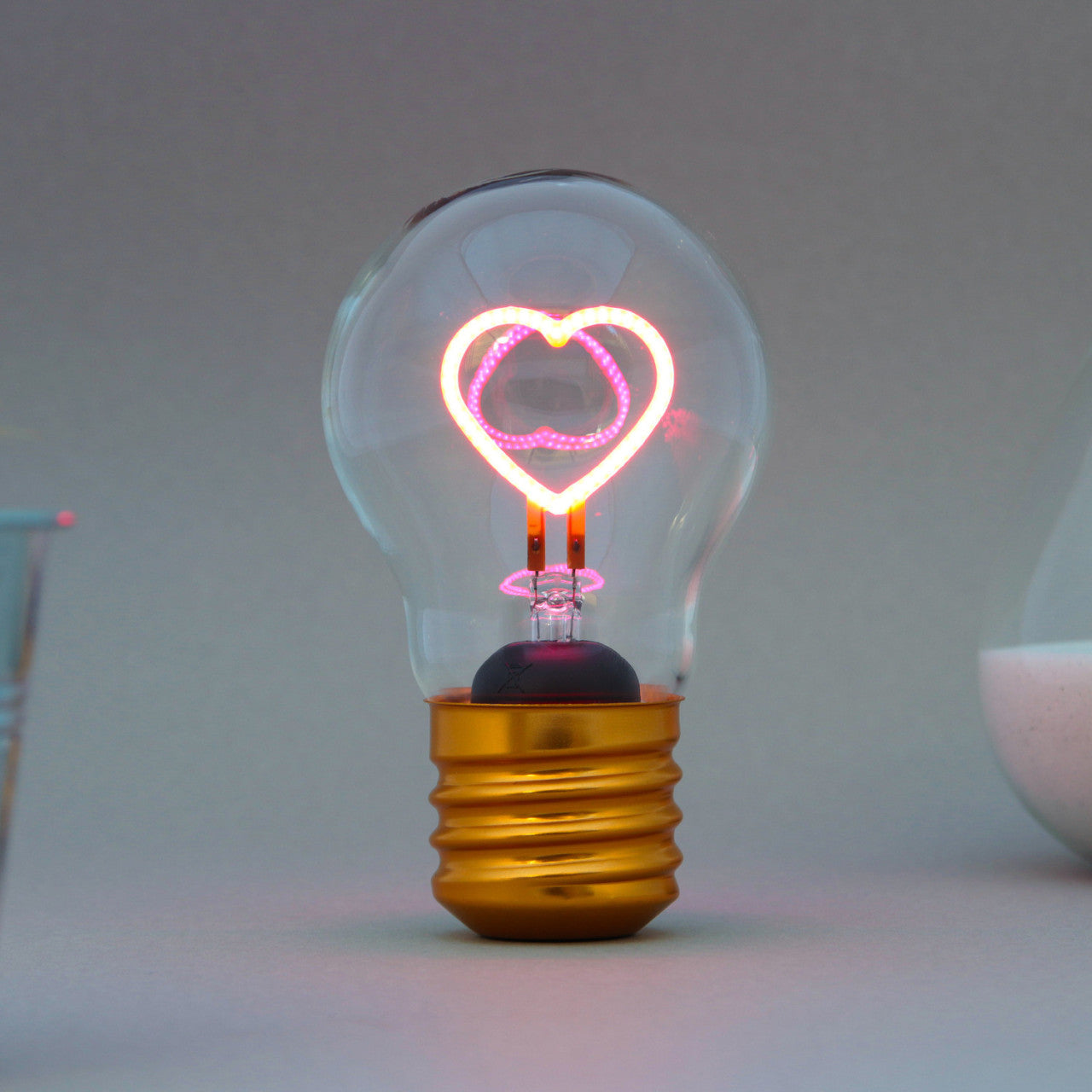 Die Kabellose LED-Glühbirne - Herz verfügt über einen leuchtenden rosa herzförmigen Glühfaden auf einem schlichten Hintergrund.