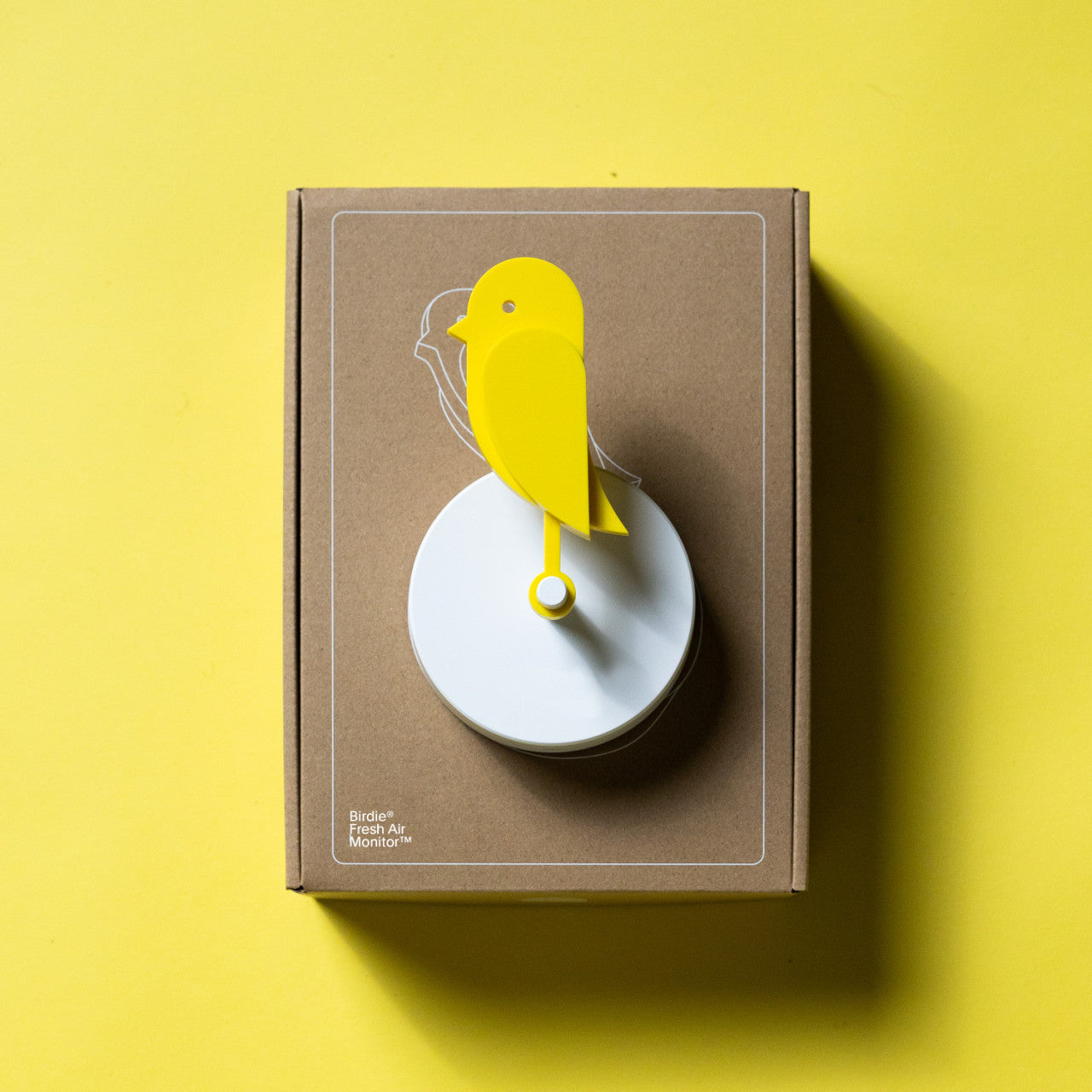 Der Frischluftmonitor Birdie 2.0 mit CO2-Sensor, ein gelbes Gerät in Vogelform, wird auf einer braunen Box mit passendem gelbem Hintergrund angezeigt.