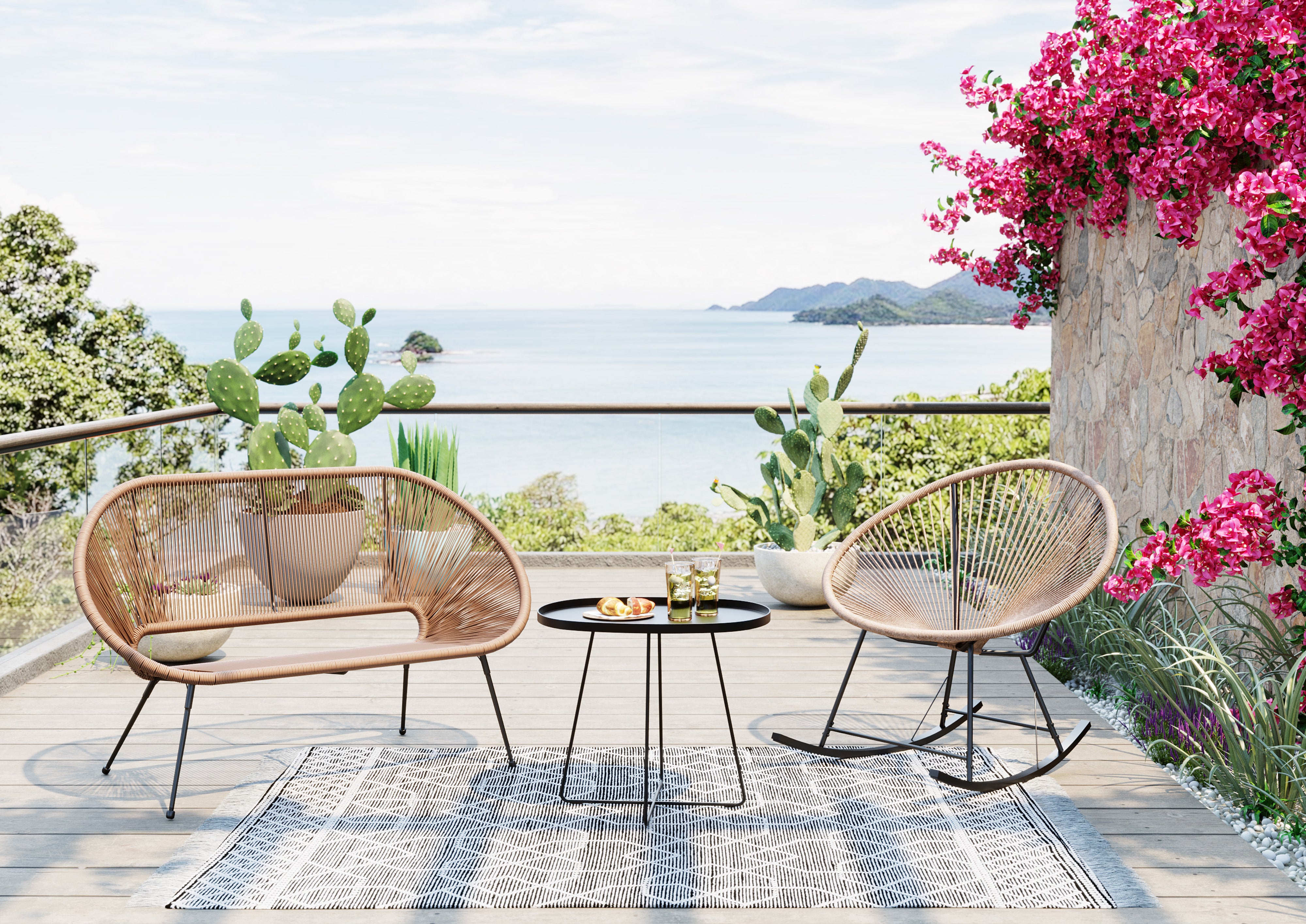 Eine Terrasse mit zwei Schaukelstühlen vom Typ Acapulco, einem kleinen schwarzen Tisch mit Getränken und Snacks, einem Teppich, Kakteen in Töpfen und leuchtend rosa Blumen bietet unter einem teilweise bewölkten Himmel Aussicht auf das Meer und die fernen Hügel.