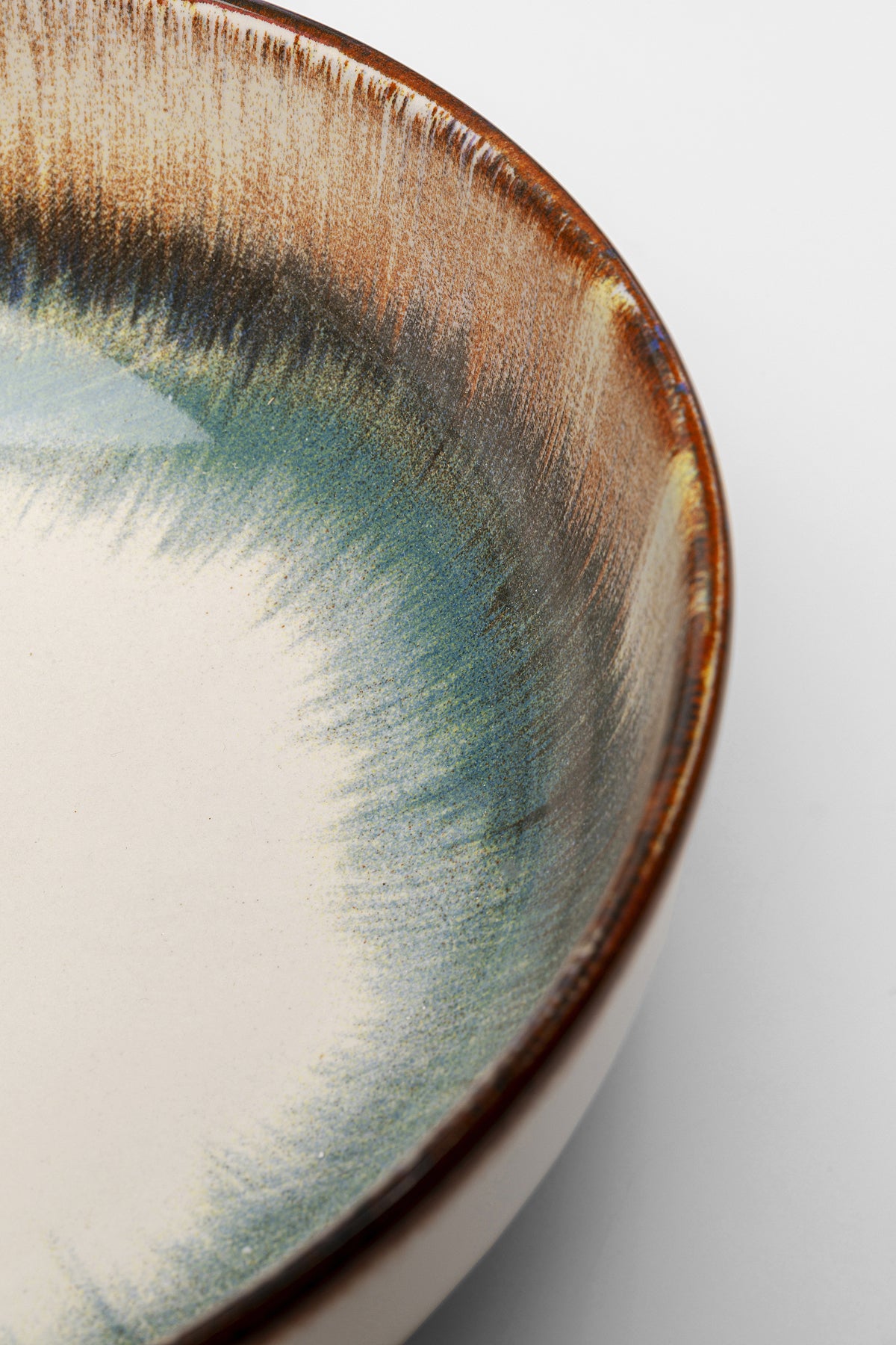 Nahaufnahme der Schüssel Laguna Blau Ø18 cm, einer Keramikschüssel mit glatter cremefarbener Innenseite und blau-brauner Farbverlaufsglasur am Rand, die die für Steinzeug Geschirr typische strukturierte, künstlerische Schönheit hervorhebt.