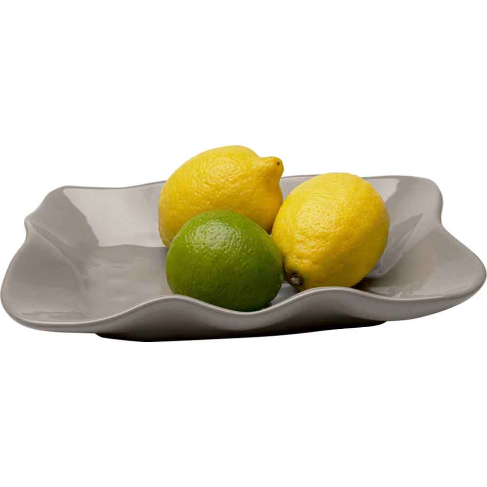 Drei Zitrusfrüchte, zwei Zitronen und eine Limette, auf einer grauen Keramikschale mit Wellenrand.