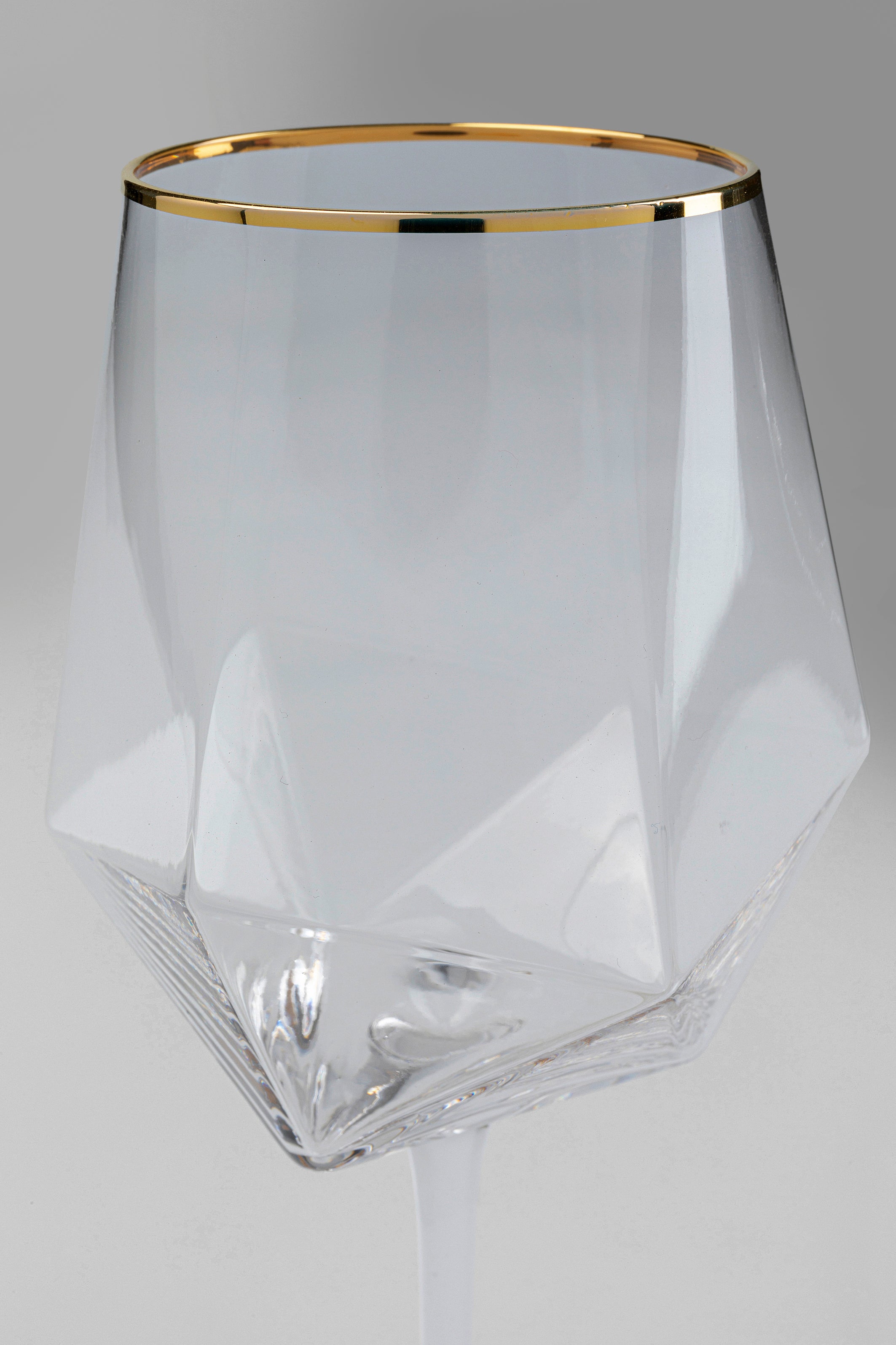 Das Weinglas Diamond Gold Rim (4/tlg.) präsentiert eine geometrische, facettierte Schale mit einem schmalen Goldrand vor einem schlichten grauen Hintergrund.