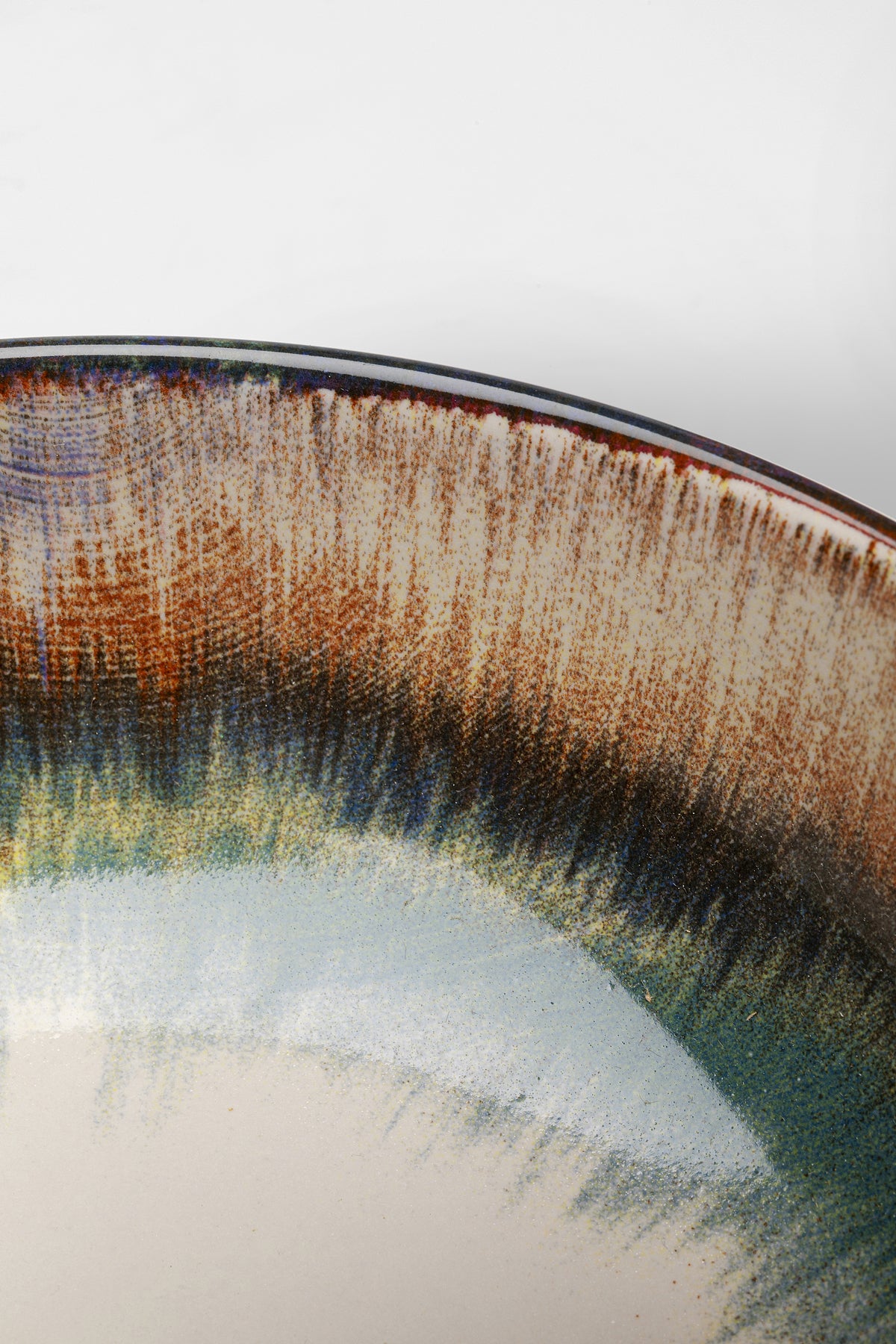 Nahaufnahme einer Schüssel Laguna Blau Ø18cm, einer Keramikschüssel mit glänzender mehrfarbiger Glasur in erdigen Braun-, Grün-, Blau- und Cremetönen und einem subtilen Farbverlaufseffekt entlang des Randes.