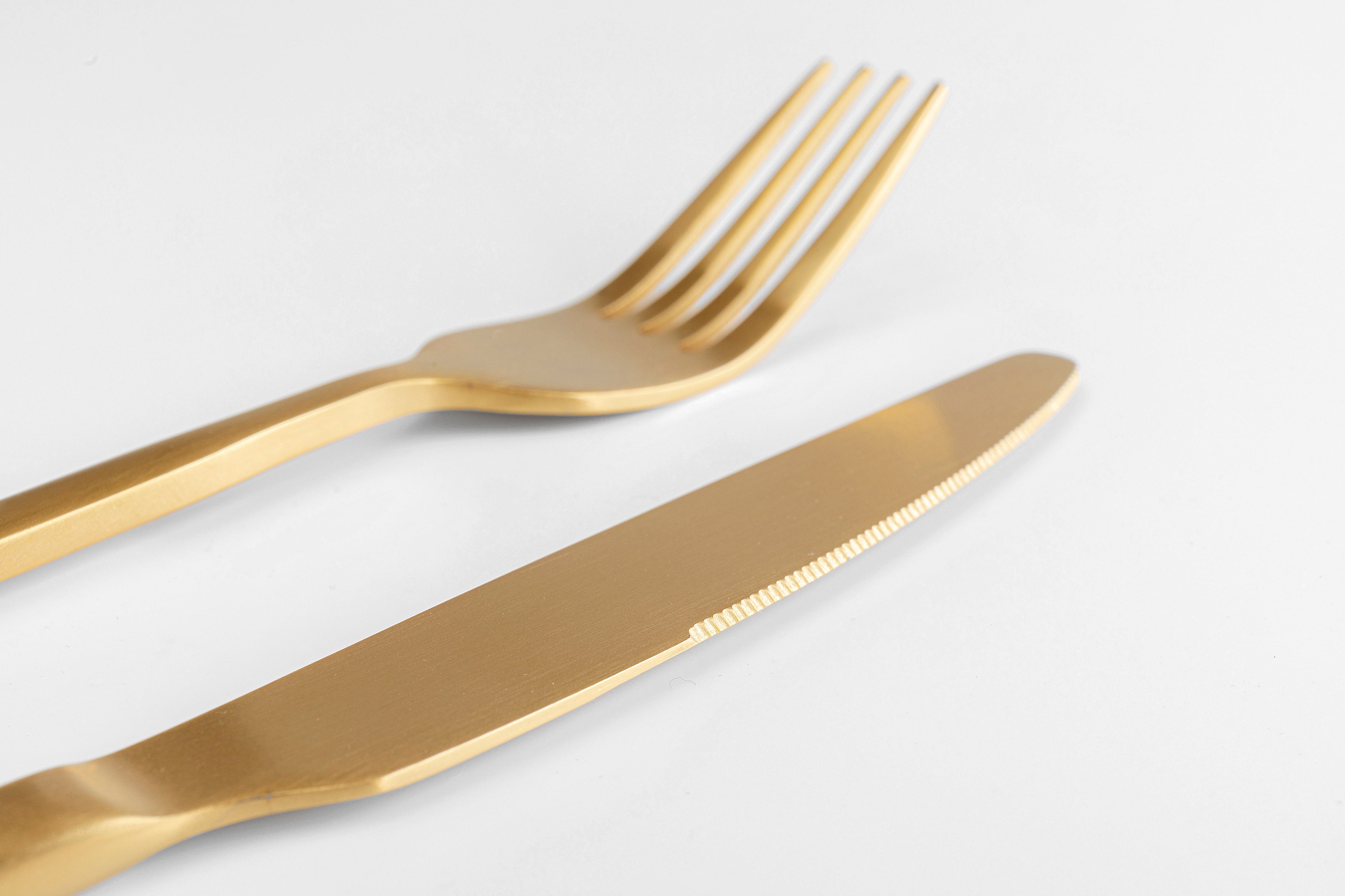Eine Gabel und ein Messer aus dem Besteck Gloria Matt Gold (16/tlg.), beide goldfarben mit mattem Finish, liegen nebeneinander auf einer weißen Fläche, wobei die Gabel über dem Messer positioniert ist.