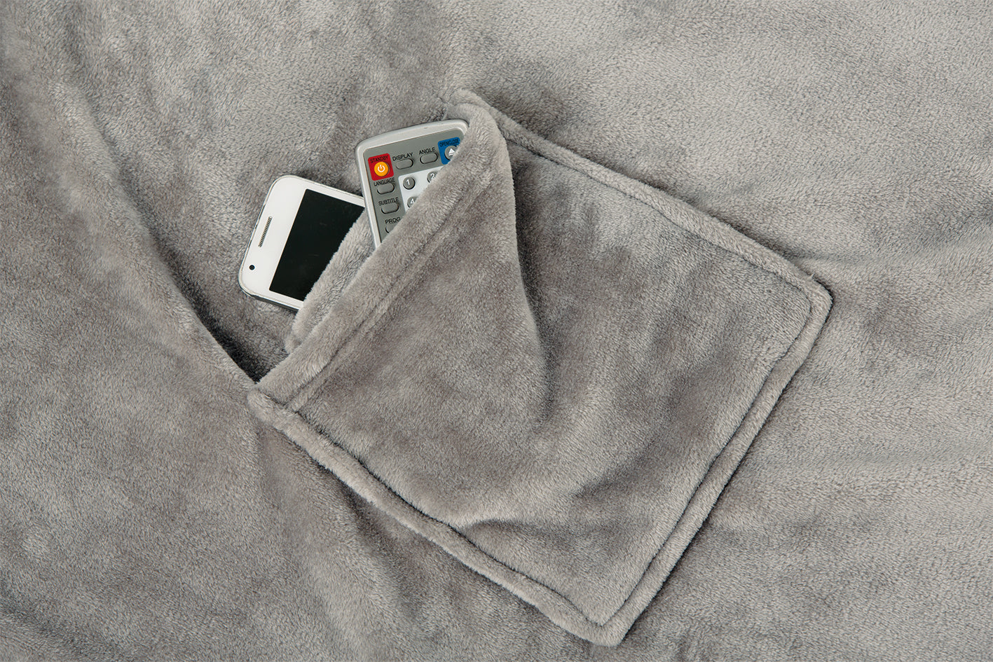 Ein weißes Smartphone und eine TV-Fernbedienung in der Tasche einer weichen, grauen Fleecedecke.