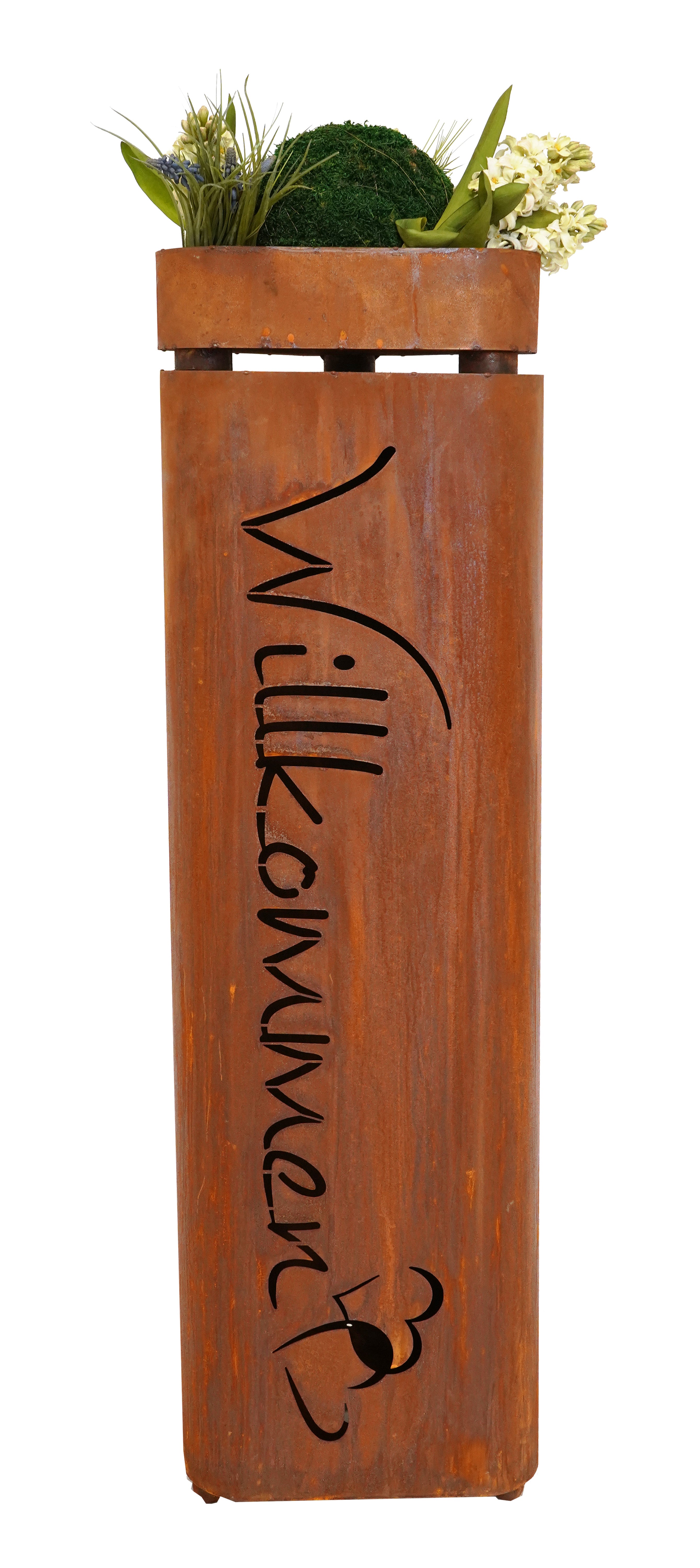 Hoher Blumentopf aus rostigem Metall mit ausgeschnittenem „Willkommen“-Text, gefüllt mit grünen Pflanzen und weißen Blumen obendrauf.