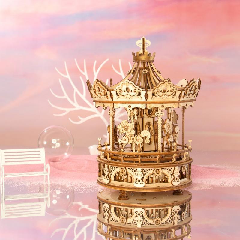 Holzkarussellmodell auf einer reflektierenden Oberfläche mit einer weißen Bank und einem pastellrosa Hintergrund.