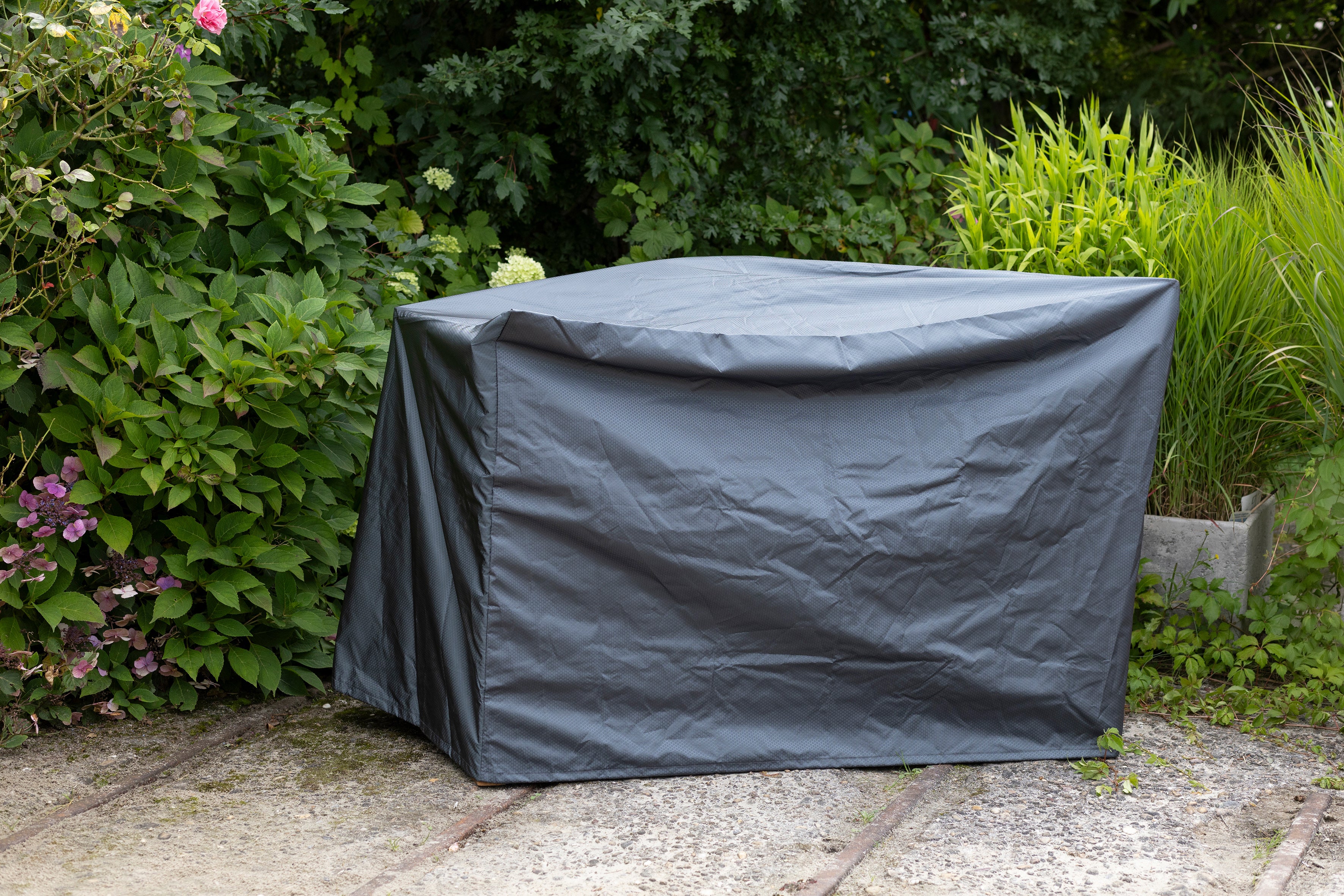 Ein großes rechteckiges Objekt, das in einer Gartenumgebung mit einer grauen Schutzplane bedeckt ist.