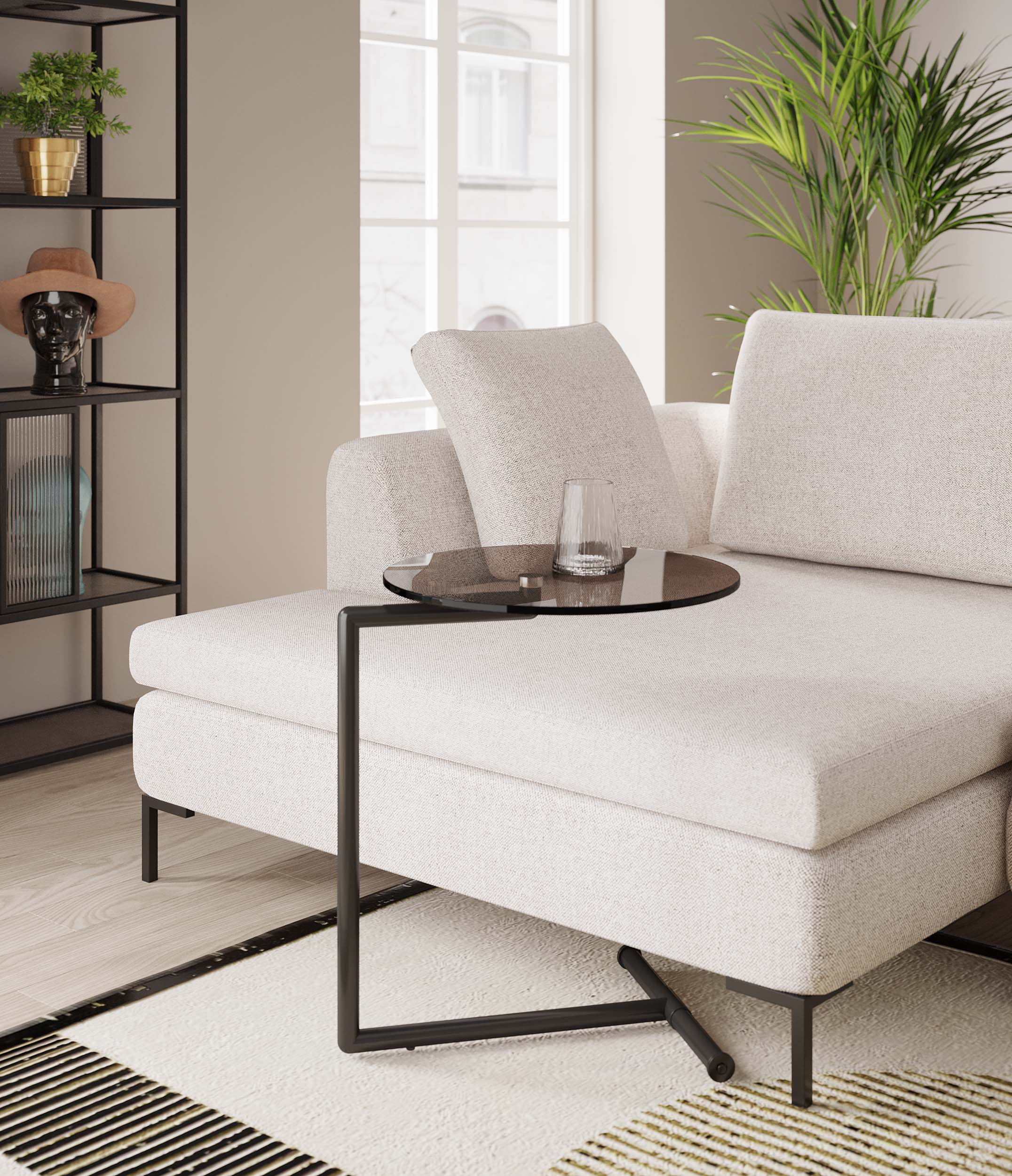 Ein modernes Wohnzimmer mit zeitlosem Design verfügt über ein hellbeiges Sofagarnitur, den Beistelltisch Easy Living Schwarz Ø46cm mit einem Glas Wasser, eine große grüne Pflanze und ein schwarzes Regal mit Dekoartikeln an der Wand.