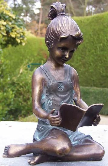 Bronzene Gartenskulptur „Lesendes Mädchen“: zeigt ein junges Mädchen, das im Garten mit verschränkten Beinen sitzt und ein Buch liest.