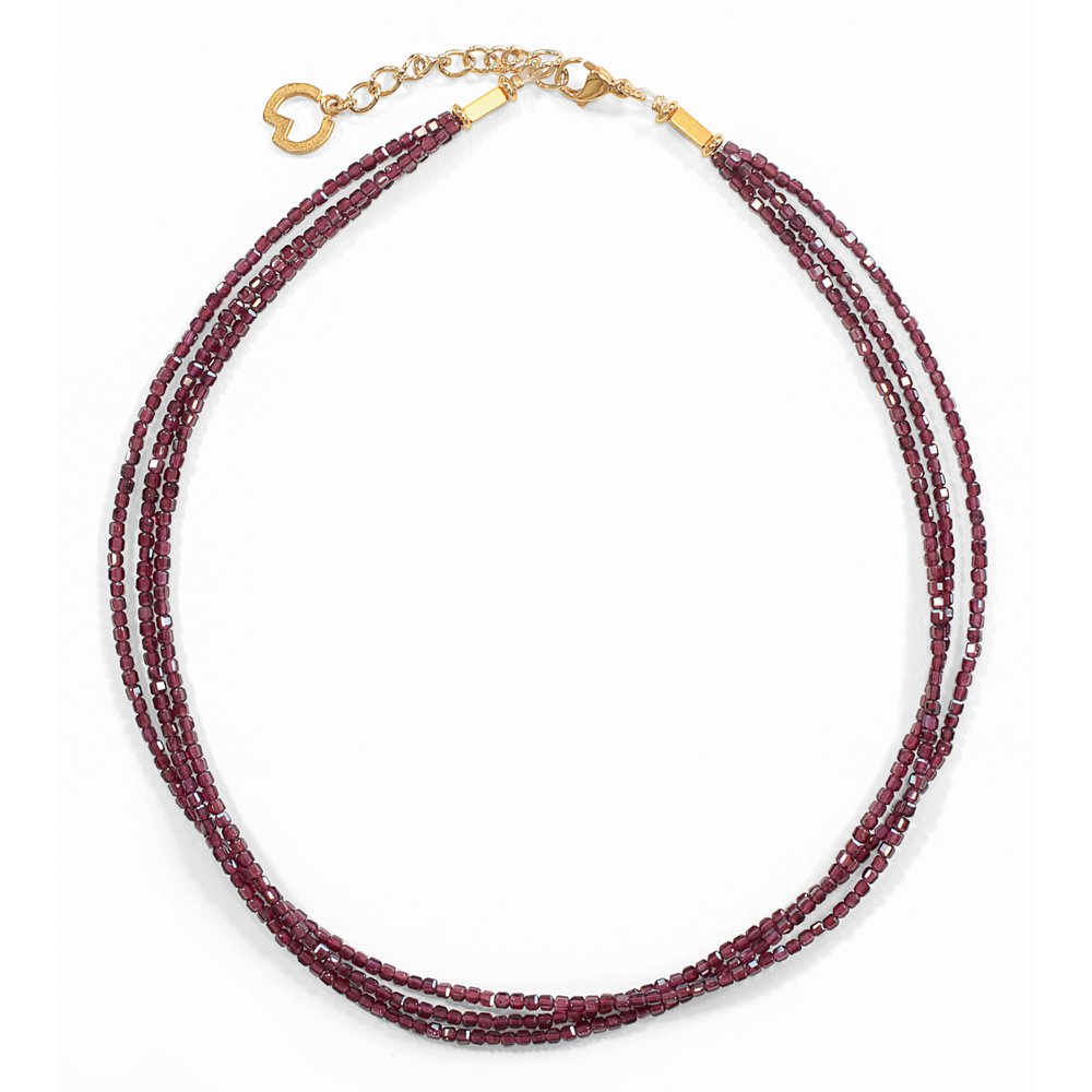 Das Petra Waszak: Collier „Garnet“ ist eine dreireihige Halskette mit kleinen tiefroten Perlen und einem goldenen Verschluss, der mit einem Herzanhänger verziert ist.