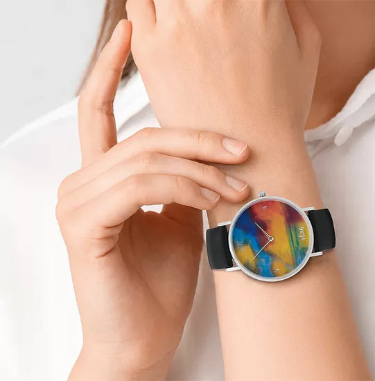 Jemand trägt die Künstler-Armbanduhr „Emil Nolde – Meer mit zwei kleinen Dampfern (rot, blau und grün)“ mit ihrem farbenfrohen abstrakten Zifferblatt und dem schwarzen Armband am linken Handgelenk.