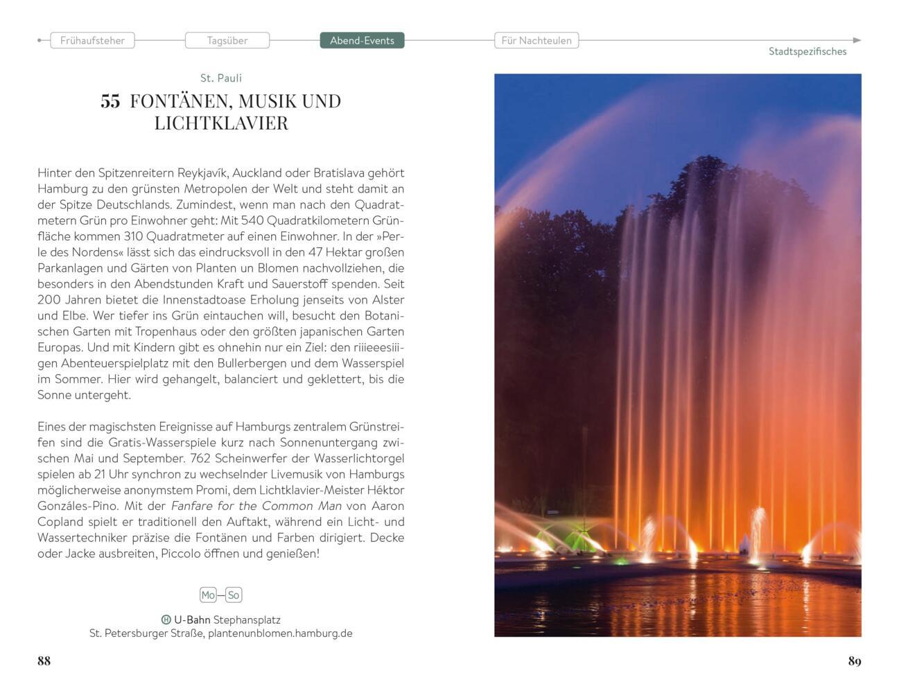 Ein großer beleuchteter Springbrunnen leuchtet nachts in einem Park orangefarben, umgeben von hohen Bäumen und einem dunklen Himmel.