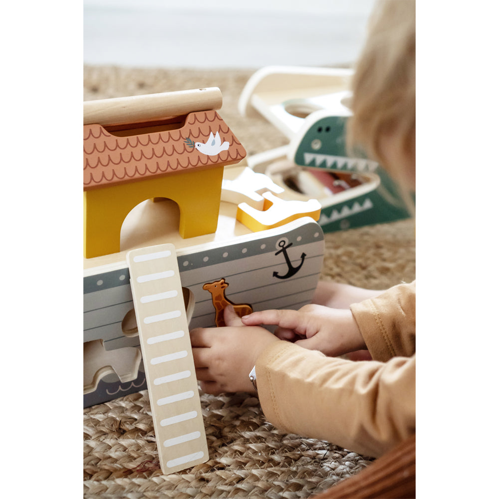 Ein Kind hat Spaß daran, mit der Steckspiel-Arche Noah „Safari“ zu spielen und Tierteile auf einem gewebten Teppich hineinzulegen.