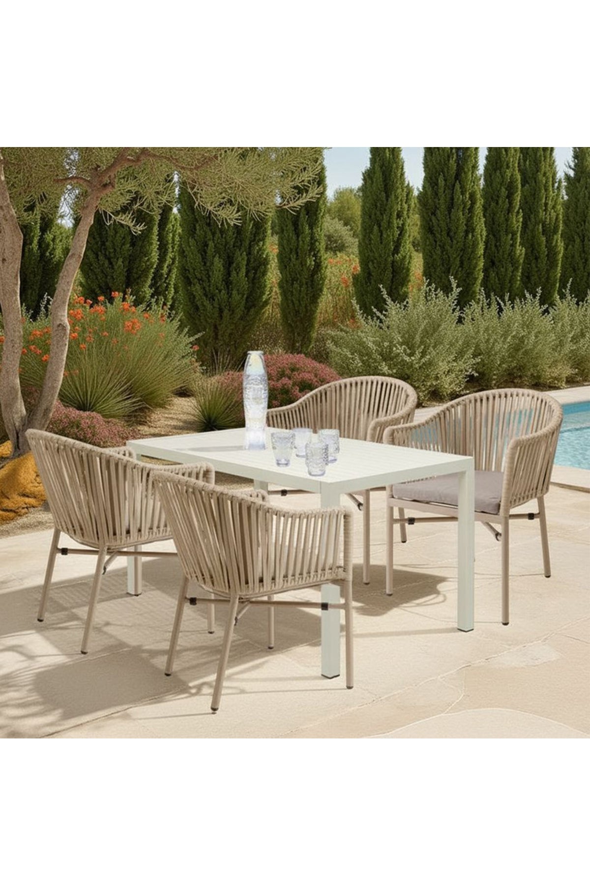 Terrasse im Freien mit einem weißen Tisch, sechs beigen Seilstühlen, einer Wasserflasche und Gläsern, neben einem Pool mit Bäumen und Pflanzen im Hintergrund.