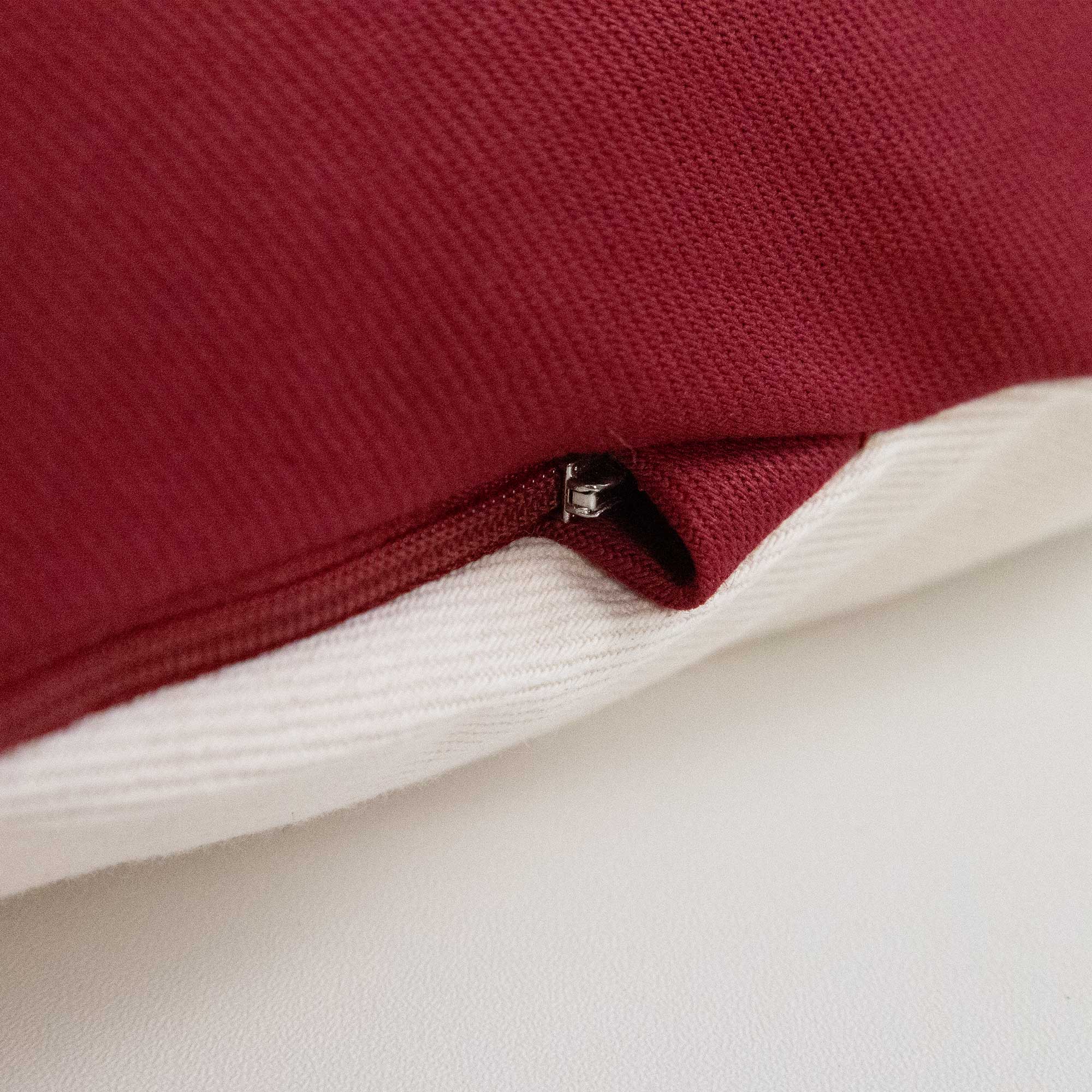 Nahaufnahme eines rot-weißen Stoffkissens mit einem teilweise sichtbaren Reißverschluss.
