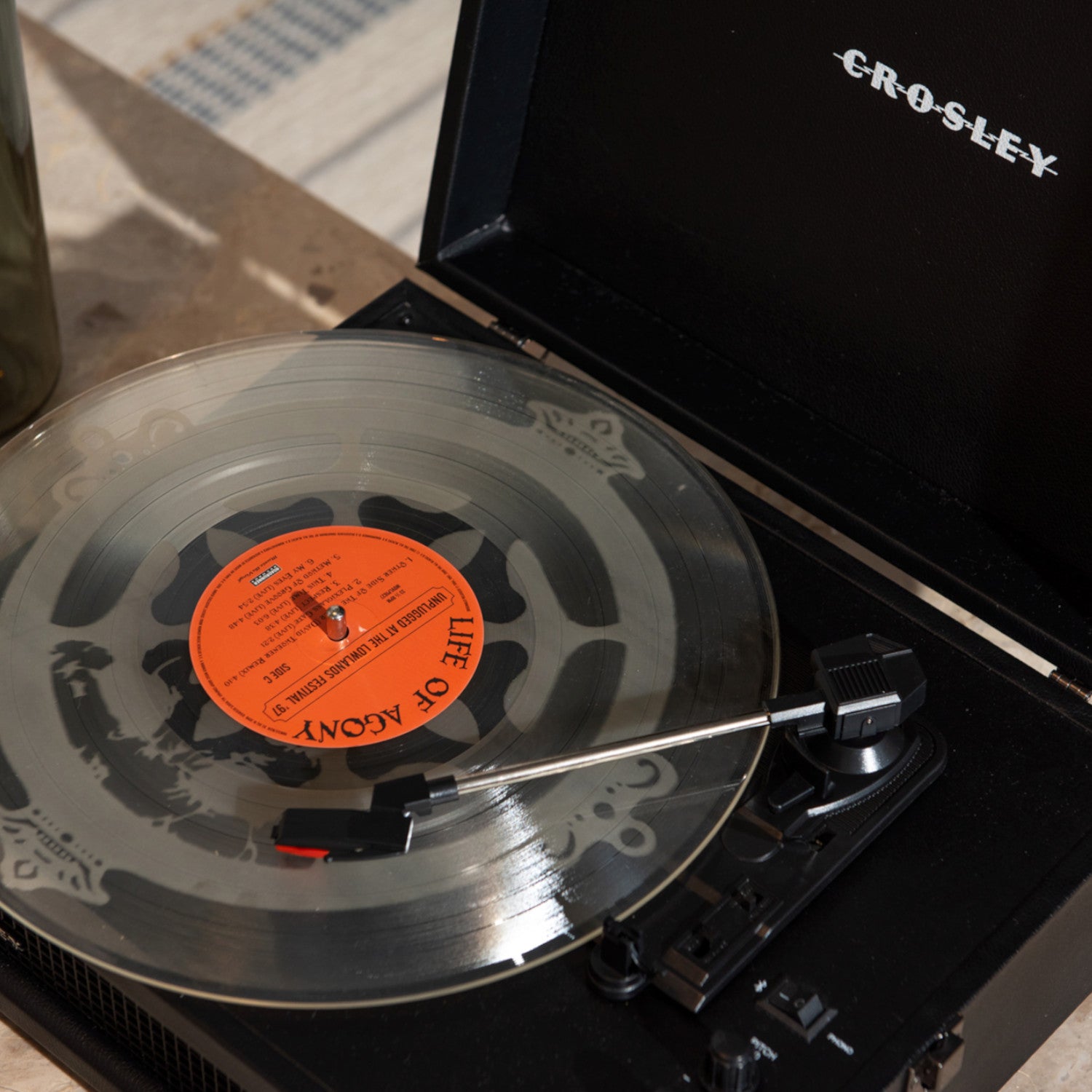 Eine durchsichtige Schallplatte auf einem Crosley-Plattenspieler; der Tonarm wird auf die sich drehende Platte gesetzt.