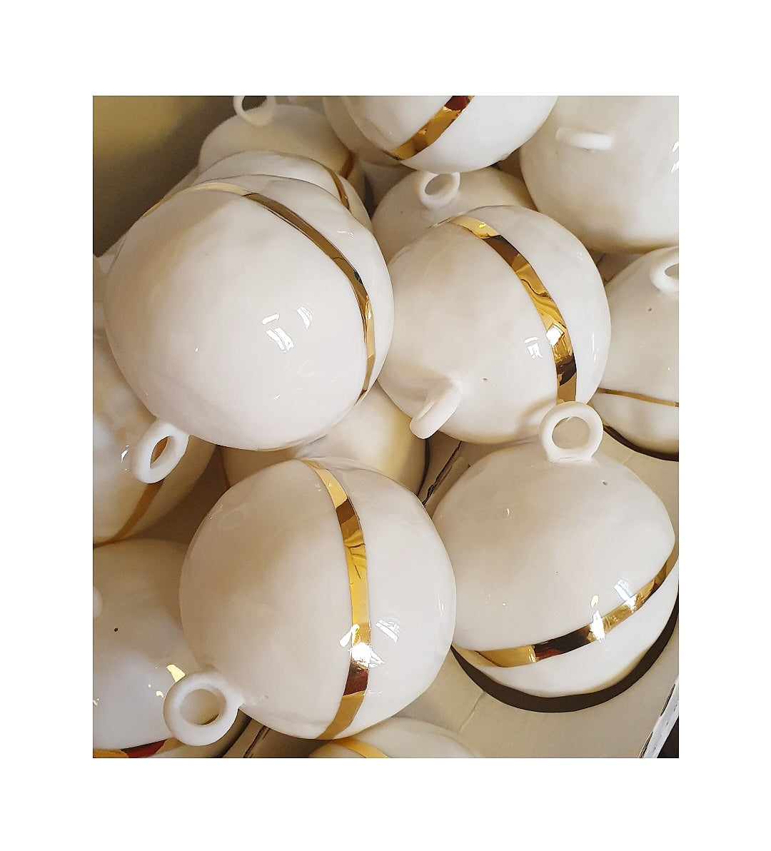 Mehrere weiße, runde Ornamente mit goldenen Bändern und kleinen Aufhängeösen, zusammen gruppiert.