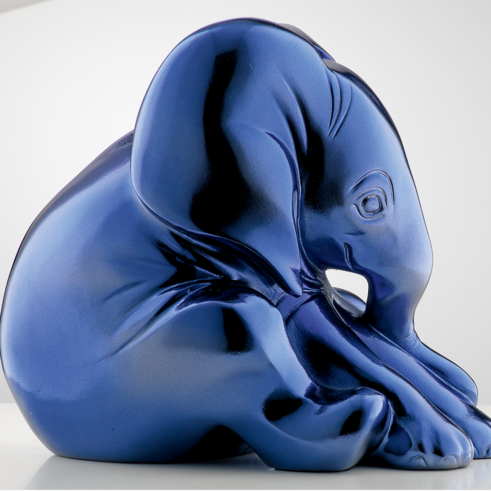 Eine leuchtend blaue Skulptur eines sitzenden Elefanten, dessen Rüssel zwischen den Vorderbeinen eingerollt ist.