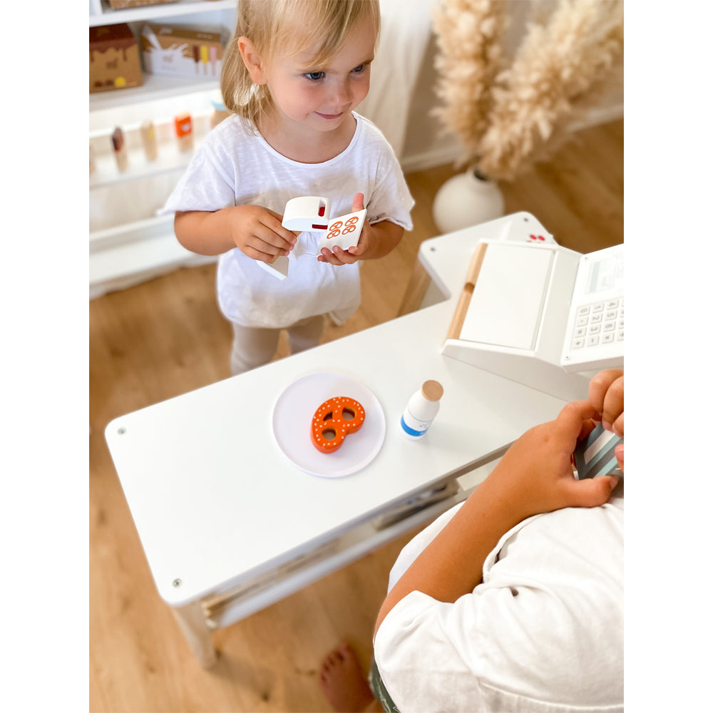 Zwei Kinder spielen mit der Spielzeugkasse „fresh“ einen Kaufladen, verwenden einen Scanner und einen Teller mit einer Spielzeugbrezel.