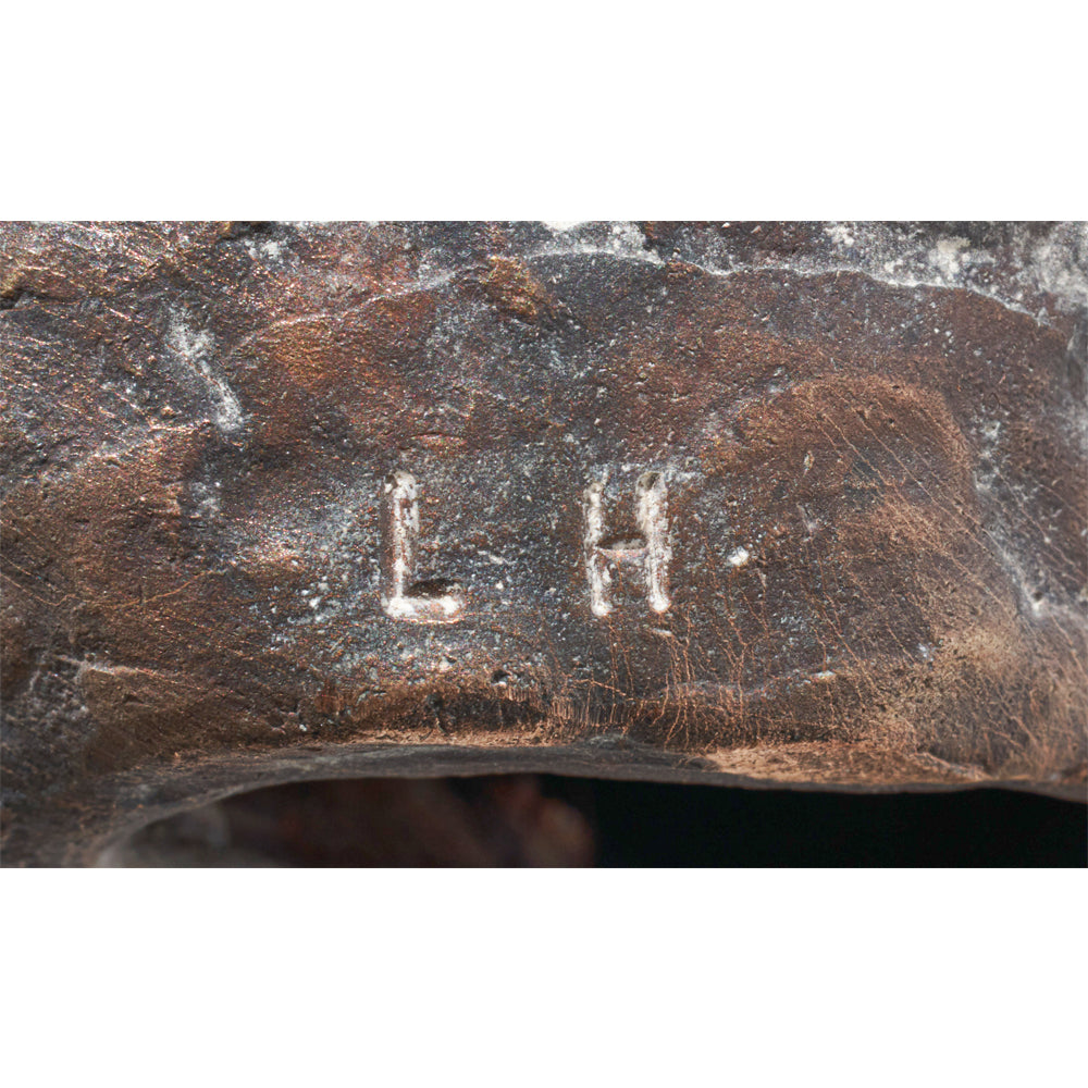 Nahaufnahme der eingravierten Buchstaben „L H“ auf der verwitterten Bronzeoberfläche von Luis Högers Skulptur „Lesende“.