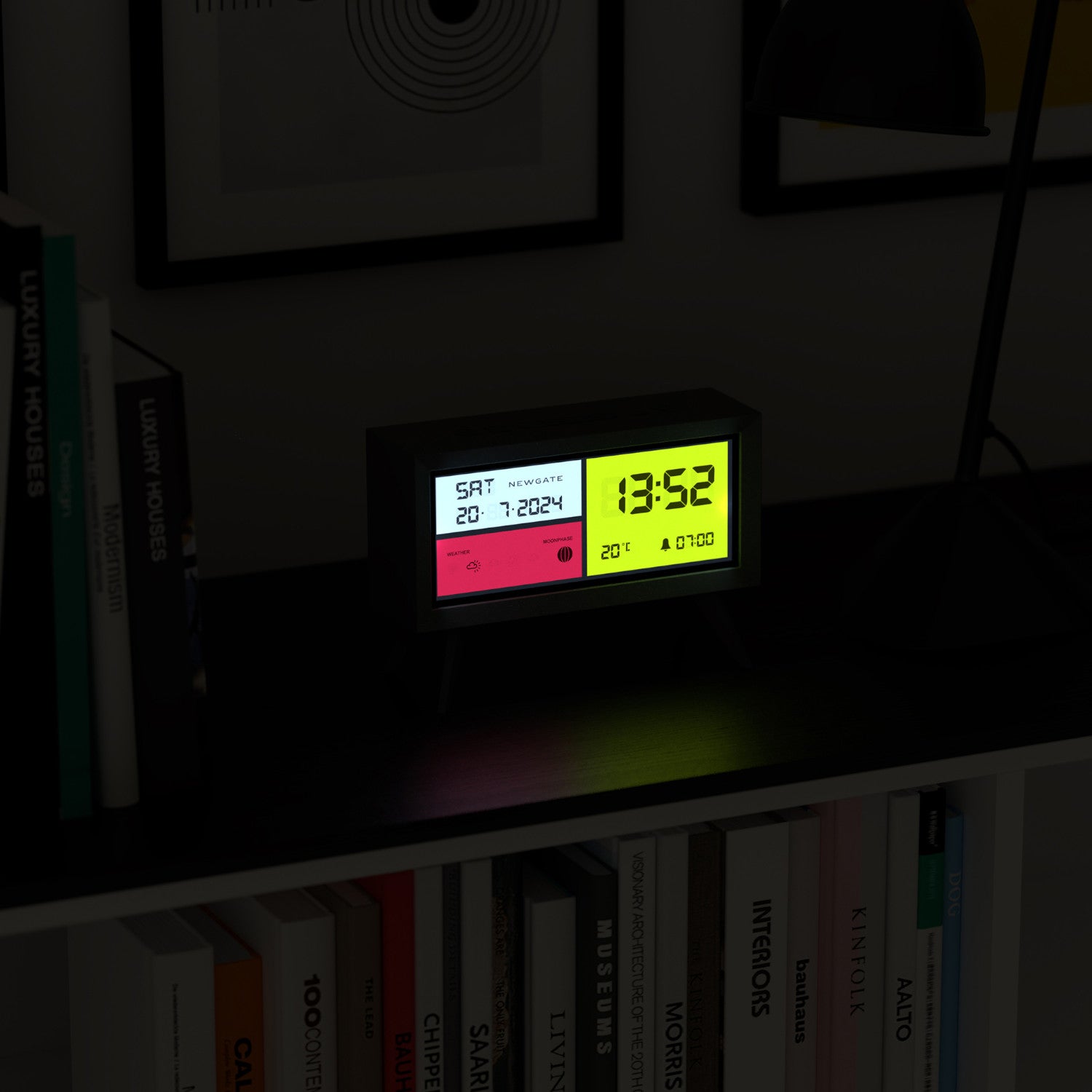 Eine Digitaluhr in einem Regal zeigt neben Büchern und gerahmten Bildern das Datum, die Uhrzeit und die Temperatur an.
