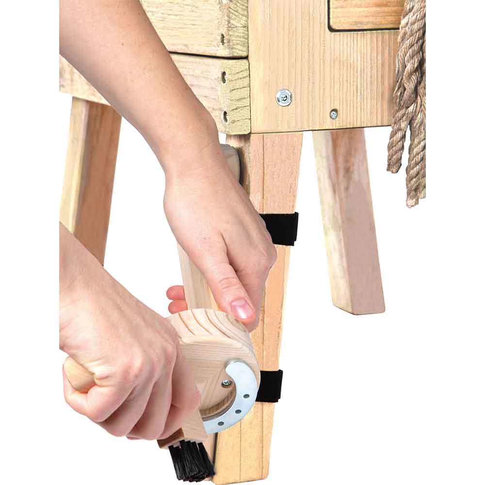 Eine Person reinigt mit einer handgeführten Holzbürste das Bein eines Holztisches oder einer Holzbank.