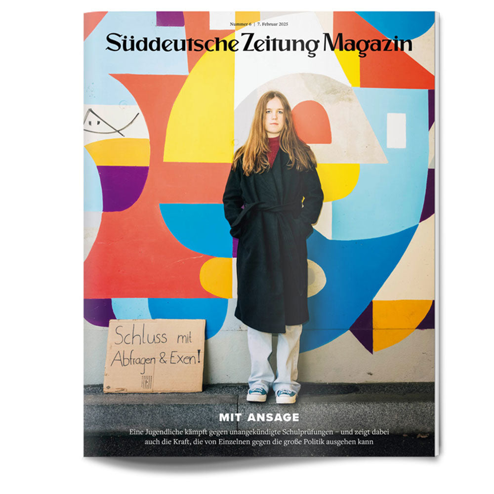 Eine junge Frau steht vor einem farbenfrohen Wandgemälde und hält ein Schild gegen Schulprüfungen in die Höhe.