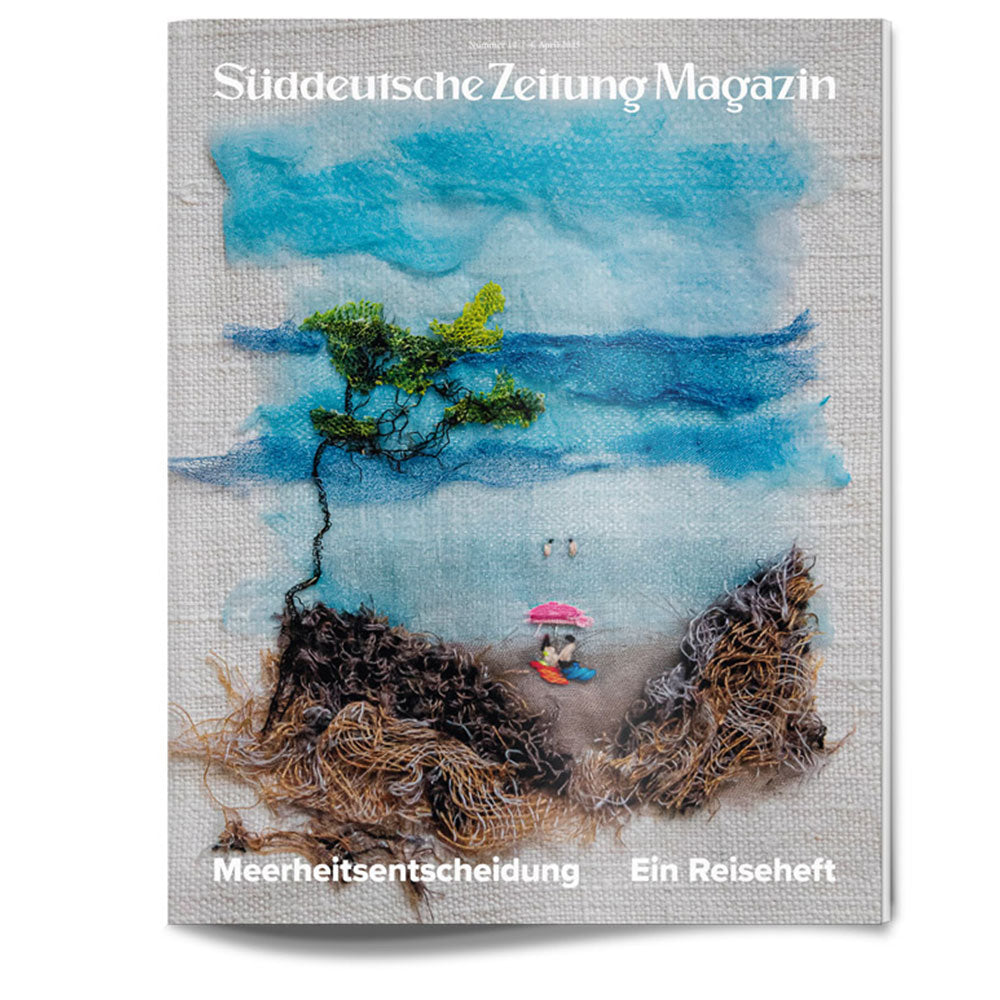 Die Titelseite des Magazins zeigt eine Strandszene mit einem Baum, dem Meer und einer Person unter einem rosa Regenschirm.