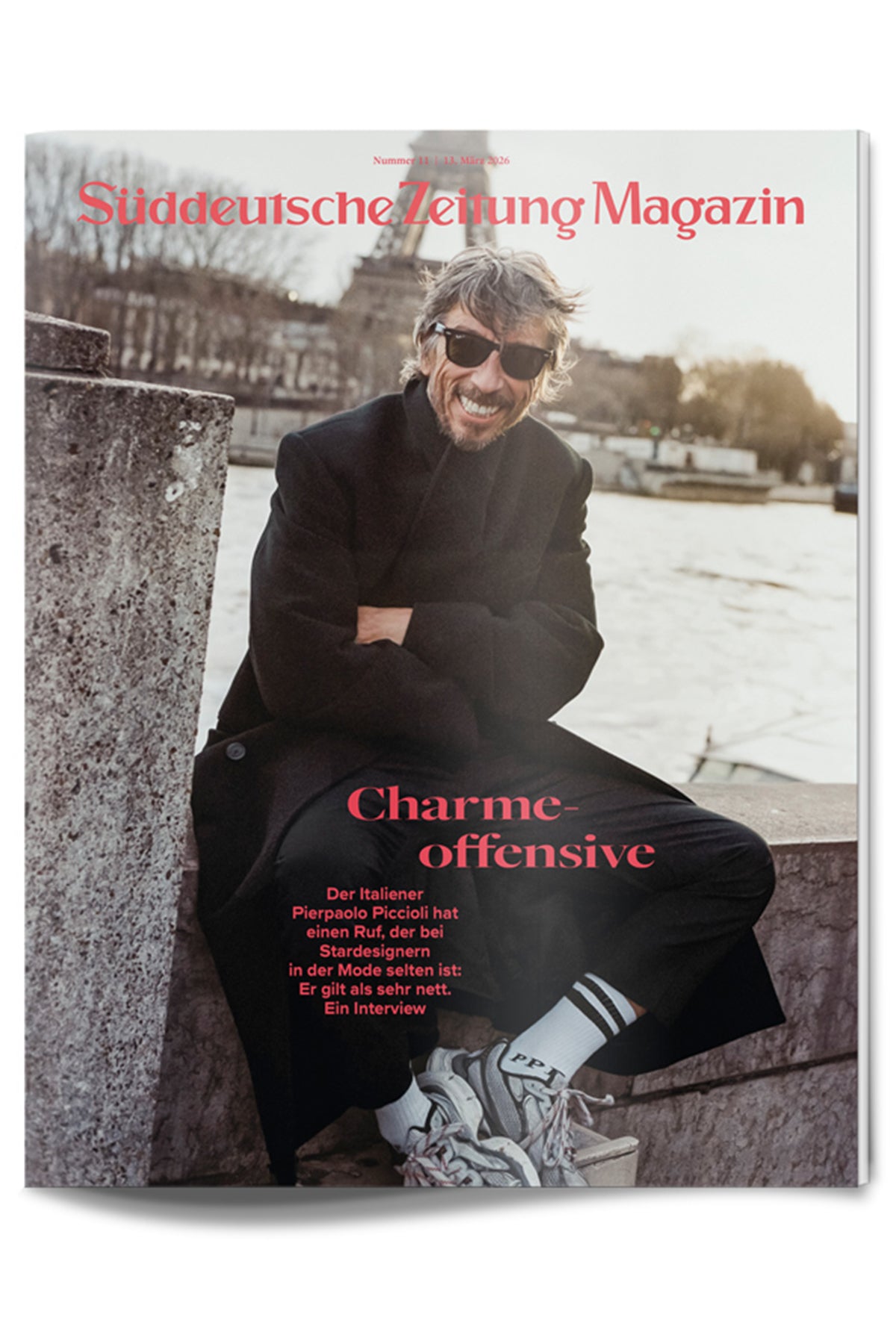 Ein Mann mit Sonnenbrille und grauem Haar sitzt lächelnd auf einem Betonvorsprung an einem Fluss und trägt einen schwarzen Mantel, weiße Socken und Turnschuhe. Der Text auf dem Cover ist auf Deutsch.