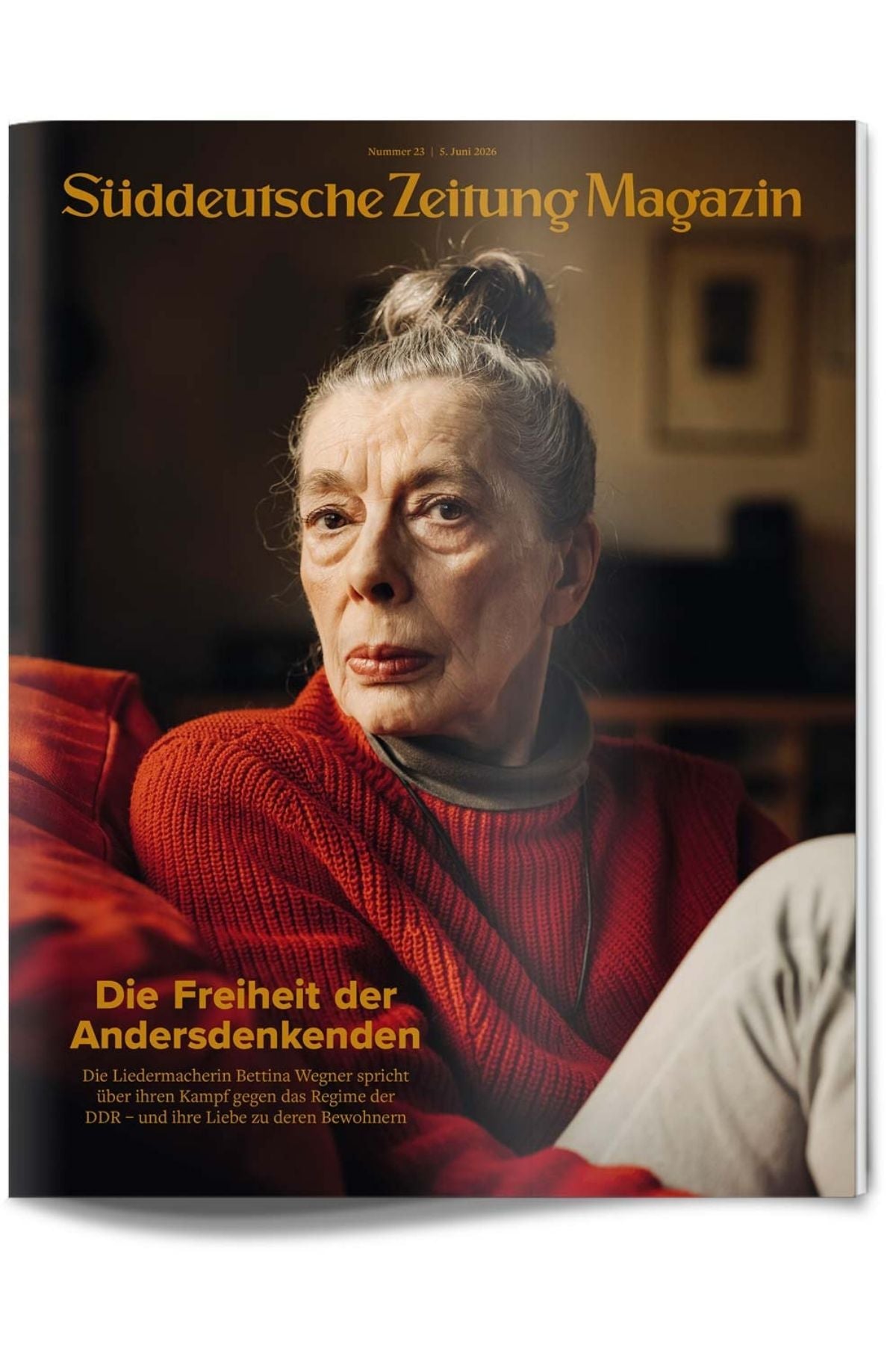 Eine ältere Frau mit grauem Haar in einem Dutt sitzt im Haus, trägt einen roten Rollkragenpullover und schaut direkt in die Kamera. Das Titelbild zeigt einen deutschen Text und einen gelben Zeitschriftentitel.