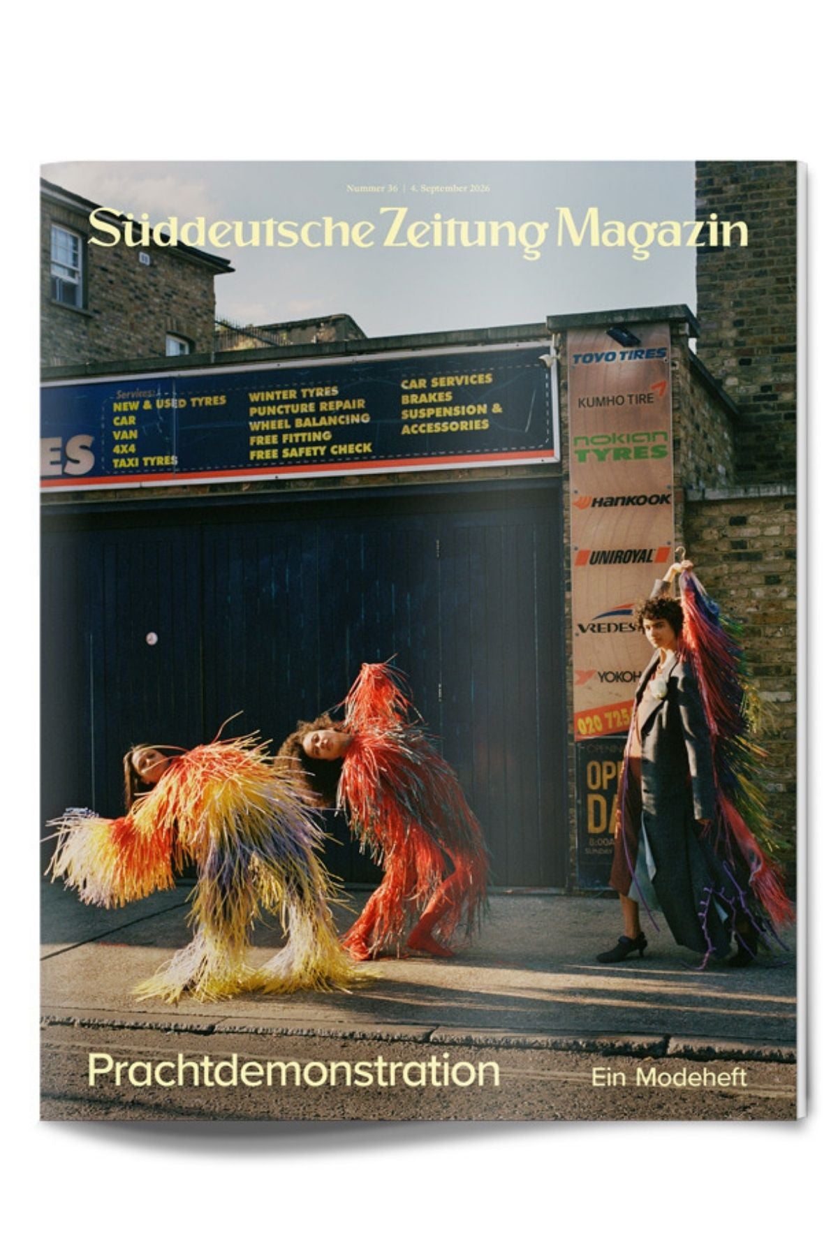 Drei Models in farbenfrohen, mit Fransen verzierten Outfits posieren auf einer Straße vor einem Reifenhändler; Titelseite des „Süddeutsche Zeitung“-Magazins, September-Ausgabe.
