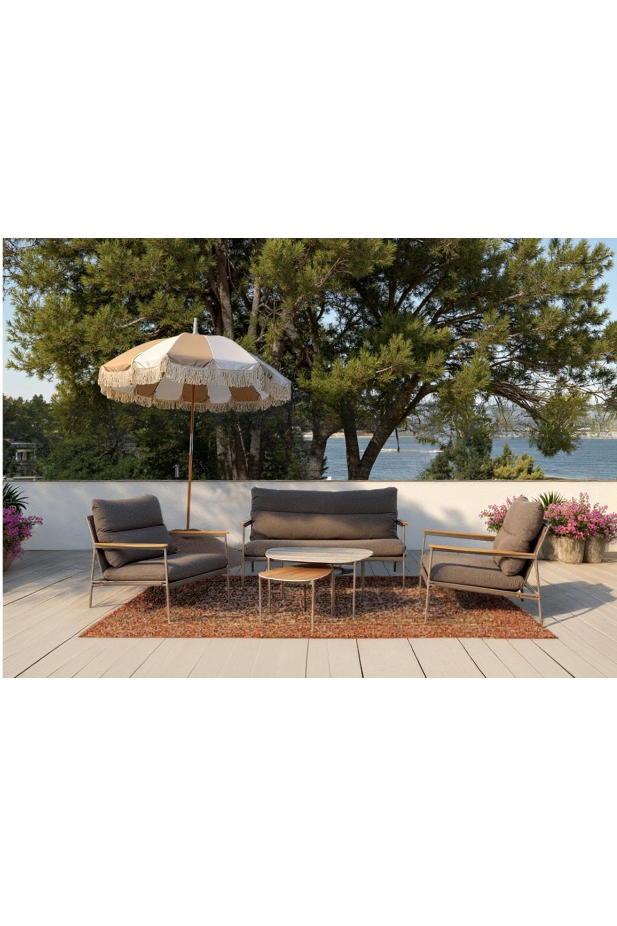 Terrassenset mit gepolsterten Stühlen, Sessel, Couchtischen, Sonnenschirm und Topfpflanzen auf einer Terrasse mit Blick auf Bäume und Wasser im Hintergrund.