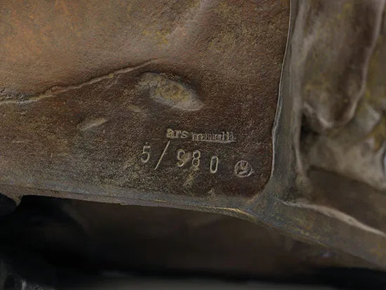 Nahaufnahme eines Sockels einer Bronzeskulptur mit eingravierter ars mundi 5/980 und einem kleinen runden Symbol.