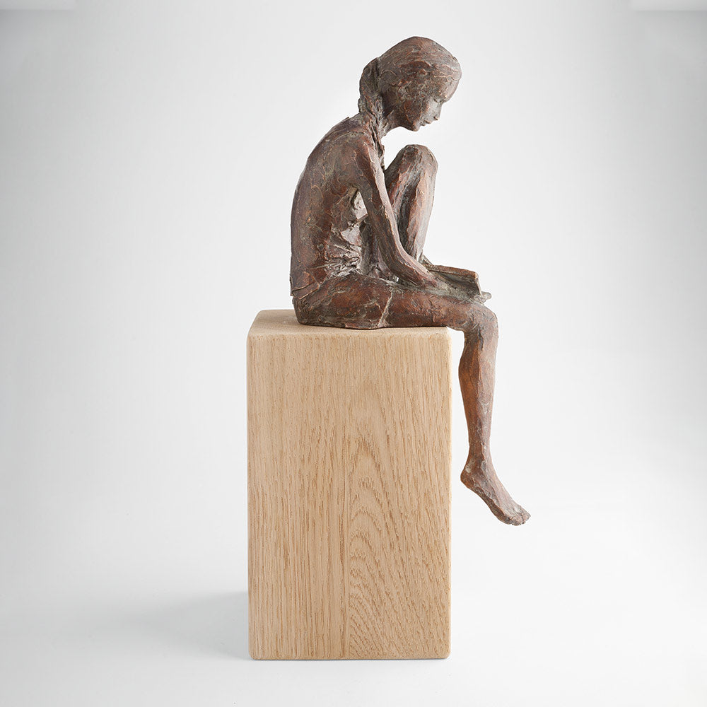 Bronzeskulptur von Valerie Otte mit dem Titel „Lesende“, die ein sitzendes lesendes Mädchen darstellt (ohne Eichensockel).