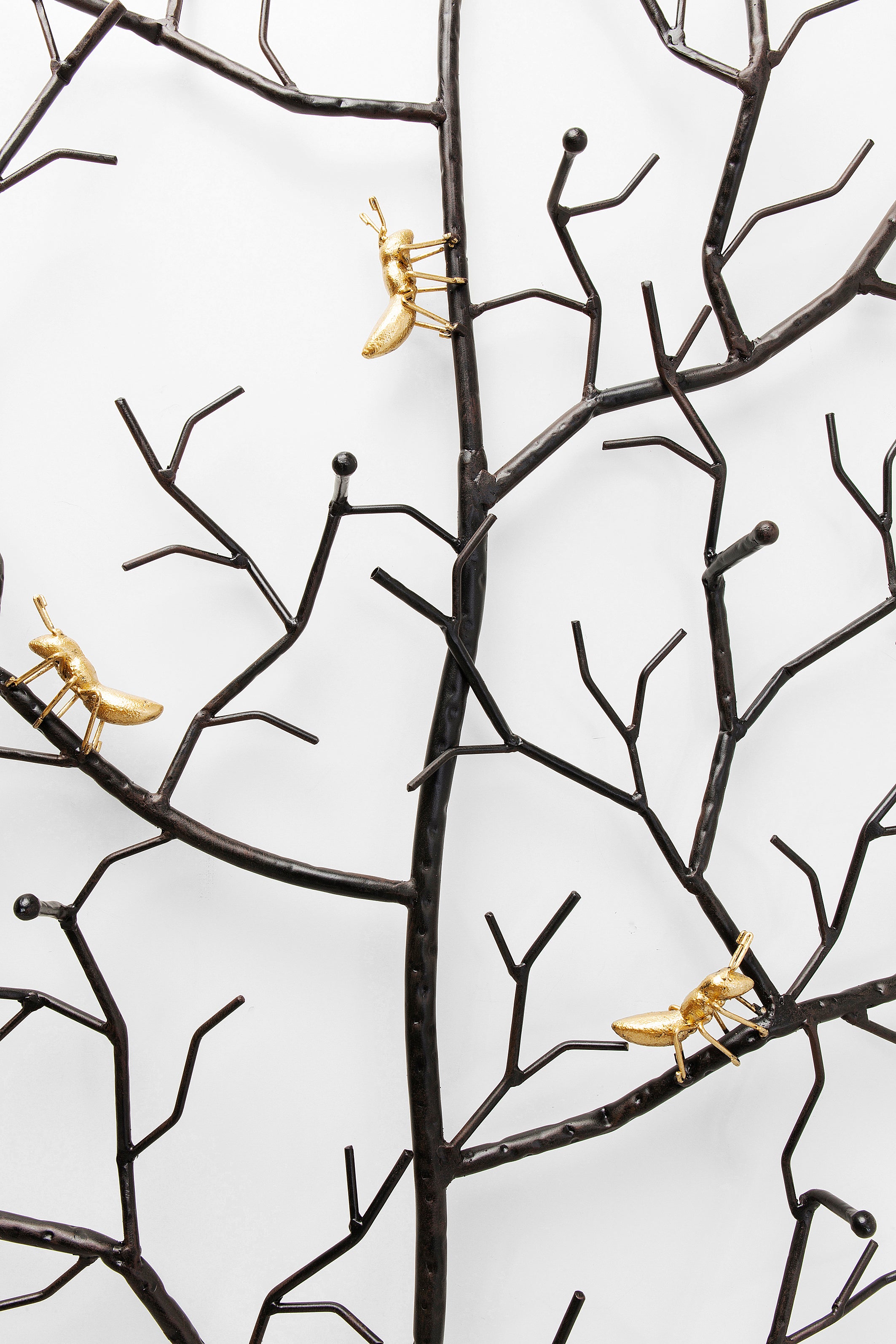 Schwarze Metallzweige mit drei kleinen, goldenen Insektenskulpturen auf den Zweigen vor einem weißen Hintergrund.