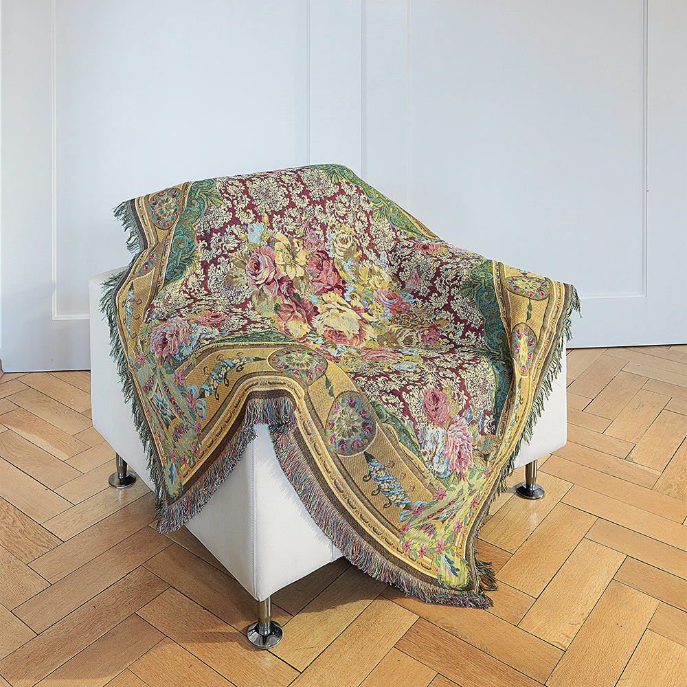 Das Wohnplaid „Aubusson“ mit farbenfrohem Blumenmuster ist über einem weißen Sessel auf einem Holzboden drapiert.