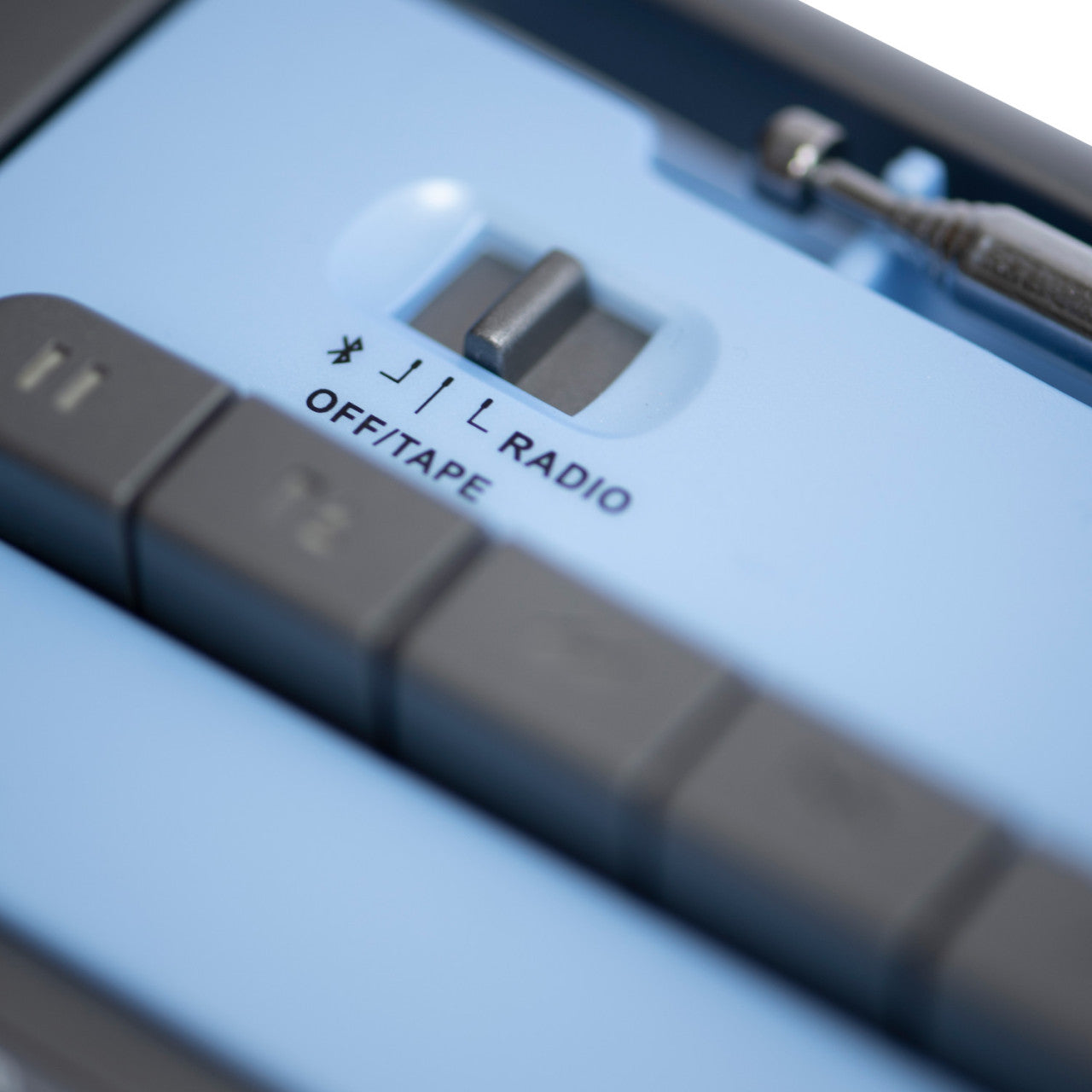Nahaufnahme eines Crosley-Kassettenspielers – Blau/Grau, mit einem Schalter mit der Aufschrift „OFF/TAPE“ und „RADIO“ neben den Tasten.