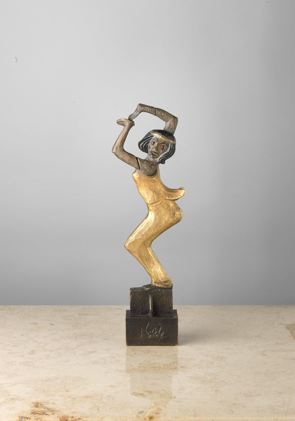 Eine stilisierte Skulptur einer tanzenden Frau aus Gold und Bronze auf einer Marmoroberfläche mit schlichtem grauem Hintergrund.