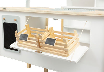 Zwei Holzkörbe mit kleinen Kreidetafelschildern auf einem weißen Regal, aus dem Kaufladen und Kinderküche Frische Spielküchen-Set.